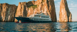 A luxury cruise ship sailing near the iconic Kicker Rock in the Galápagos Islands at sunset